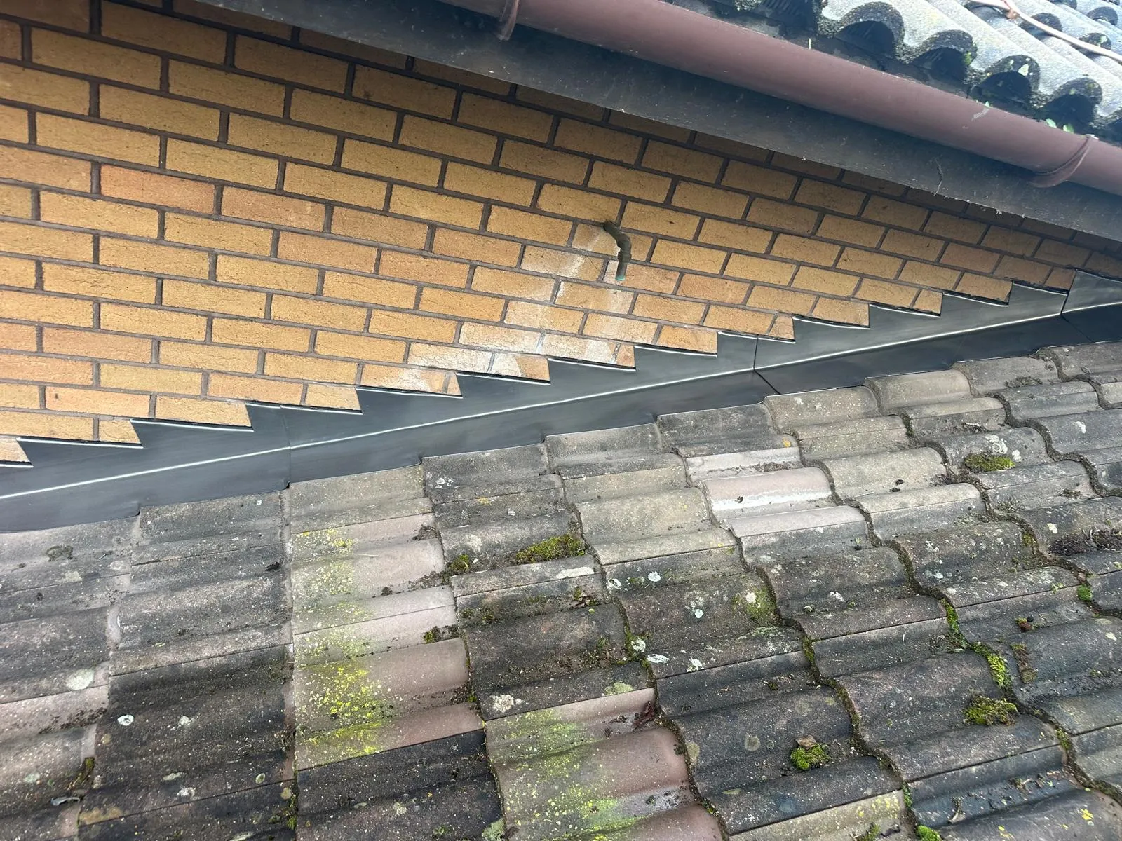 Freshly dressed stepped lead flashing where a pitched roof meets a brick wall