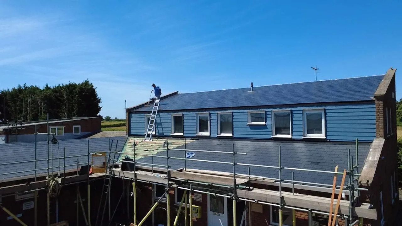 Natural slate re-roof under way, with scaffolding and a clear blue sky